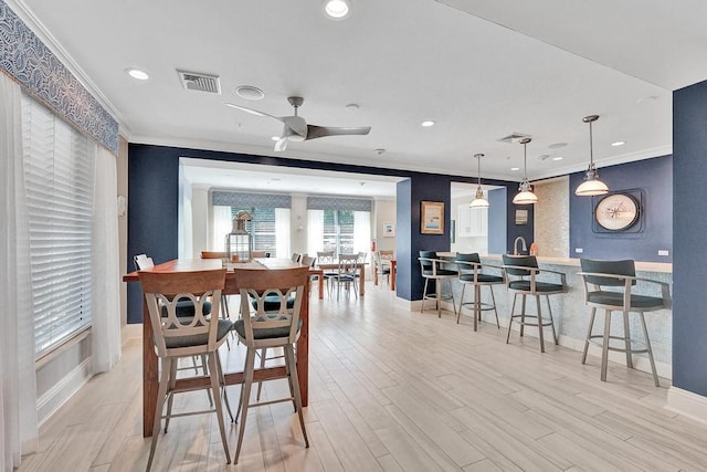 dining area featuring ceiling fan, ornamental molding, and light wood-type flooring