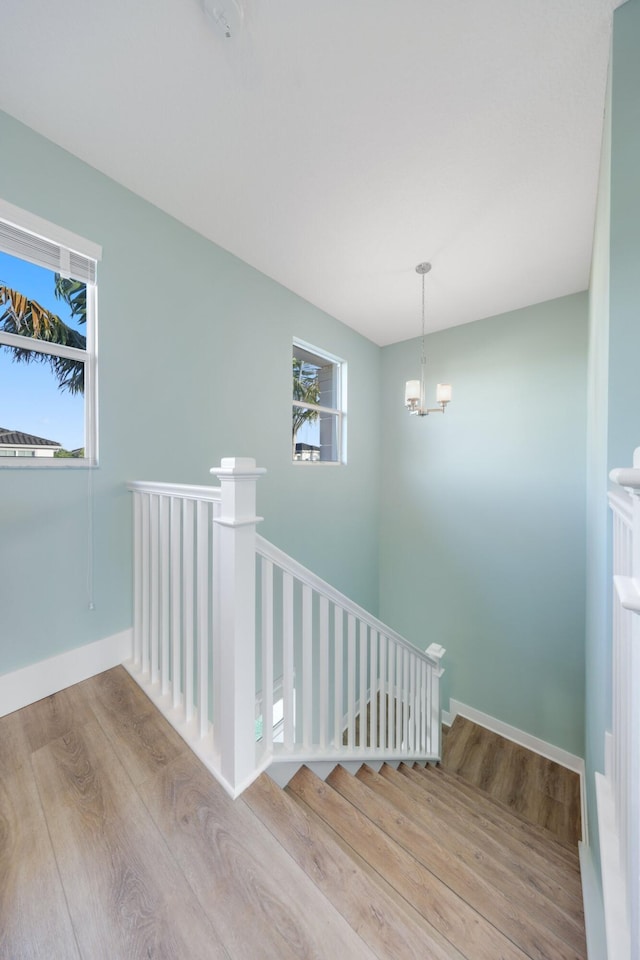 stairway with baseboards, wood finished floors, and an inviting chandelier