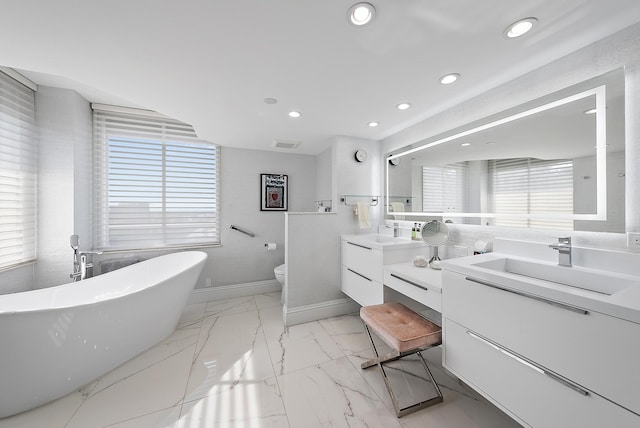 bathroom featuring vanity, a tub to relax in, toilet, and plenty of natural light