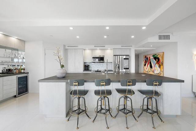 kitchen featuring a kitchen bar, appliances with stainless steel finishes, decorative backsplash, beverage cooler, and light tile patterned flooring