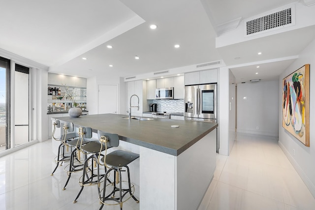 kitchen with a breakfast bar, backsplash, a large island with sink, sink, and appliances with stainless steel finishes