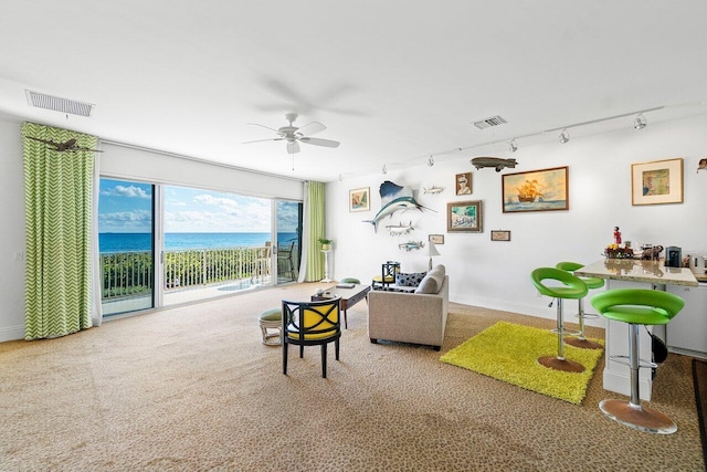 carpeted living room with ceiling fan, a water view, and track lighting