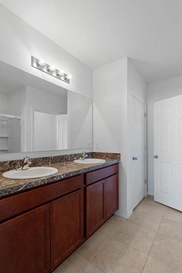 bathroom with tile patterned flooring, vanity, a shower with door, and a textured ceiling