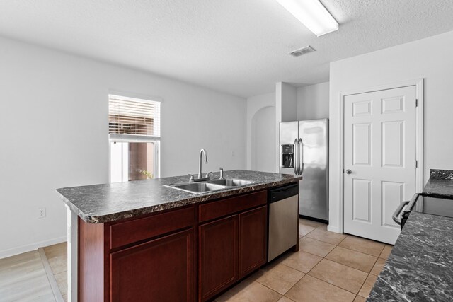 kitchen featuring a center island with sink, sink, light tile patterned floors, a textured ceiling, and appliances with stainless steel finishes