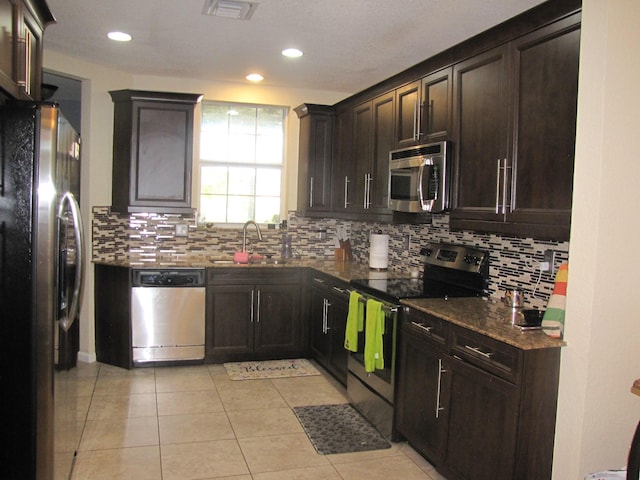 kitchen with dark stone counters, sink, light tile patterned floors, and stainless steel appliances