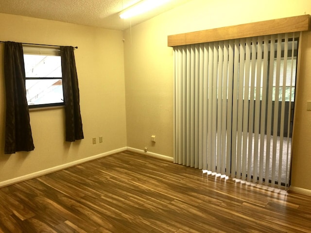 empty room featuring dark hardwood / wood-style flooring, a textured ceiling, and vaulted ceiling