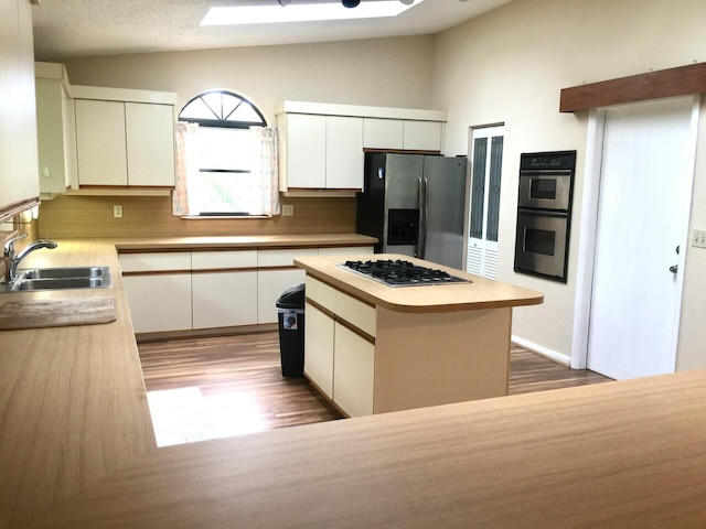 kitchen featuring appliances with stainless steel finishes, lofted ceiling with skylight, sink, a center island, and white cabinetry