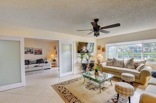 tiled living room featuring ceiling fan with notable chandelier and a textured ceiling