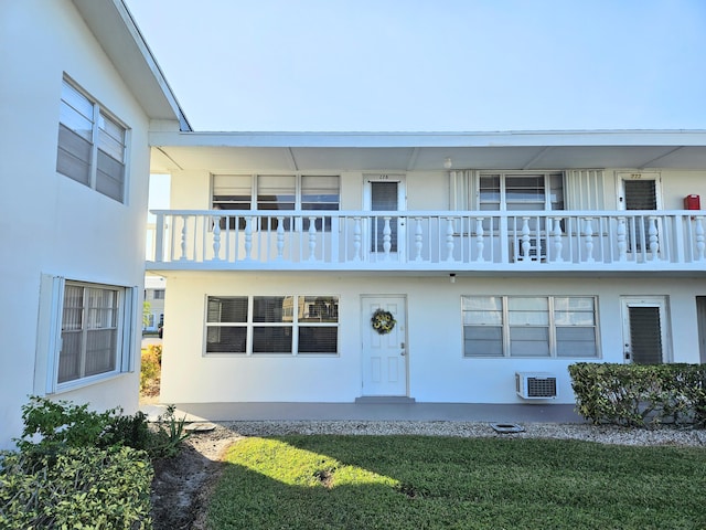 view of front of property with an AC wall unit, a balcony, and a front yard