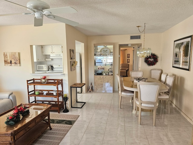 tiled dining space featuring ceiling fan with notable chandelier and a textured ceiling