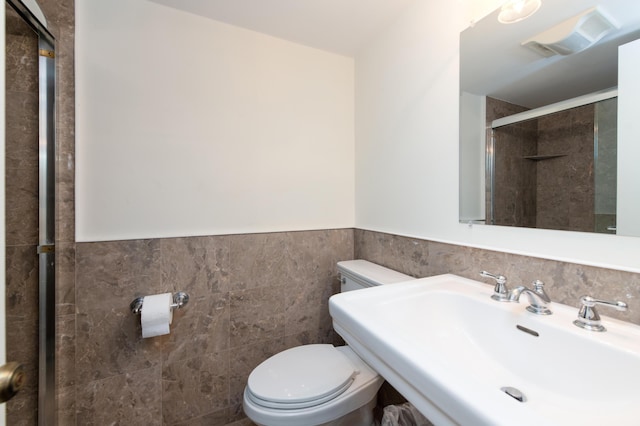 bathroom with a shower with shower door, sink, tile walls, and toilet