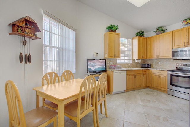 kitchen featuring appliances with stainless steel finishes, backsplash, sink, lofted ceiling, and light tile patterned flooring