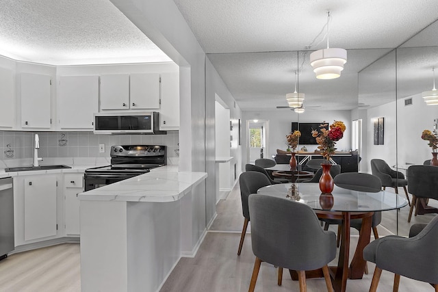 kitchen with appliances with stainless steel finishes, sink, light hardwood / wood-style flooring, white cabinetry, and hanging light fixtures