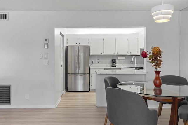 kitchen featuring stainless steel refrigerator, sink, backsplash, pendant lighting, and white cabinets