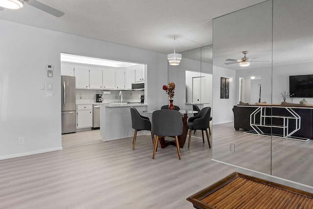 dining area with ceiling fan, sink, light hardwood / wood-style floors, and a textured ceiling