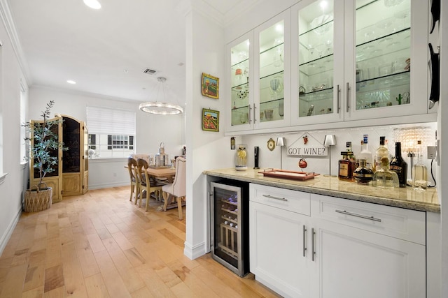 bar with light stone countertops, white cabinetry, crown molding, and wine cooler