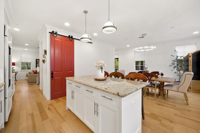 kitchen featuring a kitchen island, a barn door, light hardwood / wood-style floors, decorative light fixtures, and white cabinets