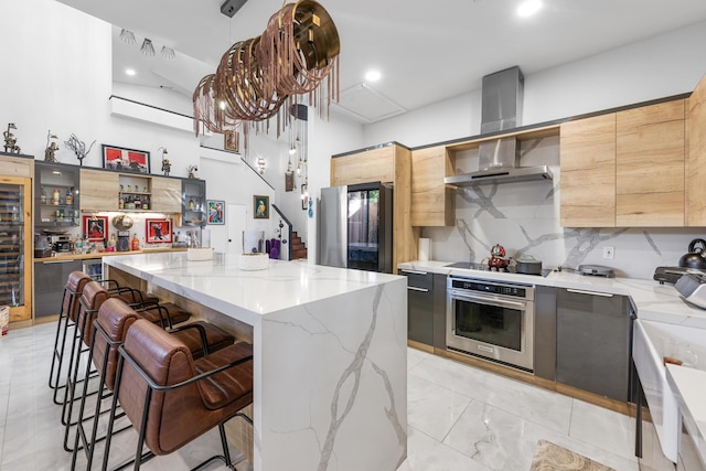 kitchen with wall chimney range hood, light stone countertops, appliances with stainless steel finishes, a kitchen island, and a kitchen bar