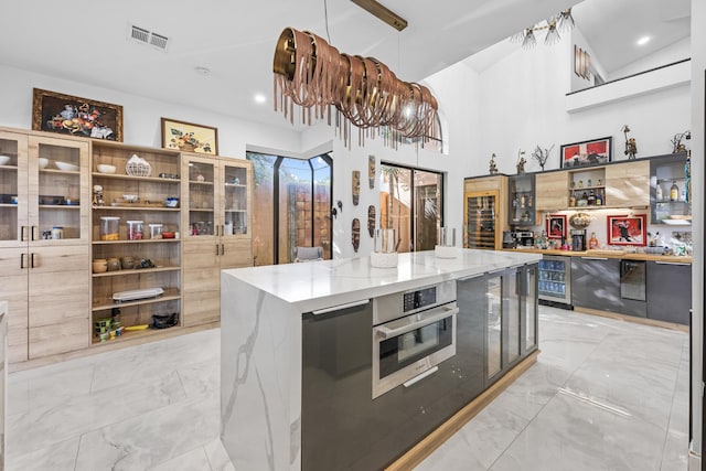 kitchen featuring beverage cooler, light stone counters, decorative light fixtures, a kitchen island, and appliances with stainless steel finishes