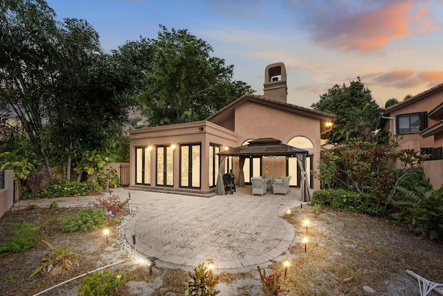 back house at dusk with outdoor lounge area, a gazebo, and a patio area