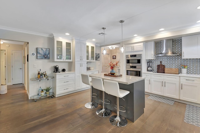 kitchen with white cabinets, wall chimney exhaust hood, light hardwood / wood-style floors, and double oven