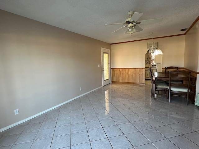 tiled dining space with a textured ceiling, ceiling fan, ornamental molding, and wood walls