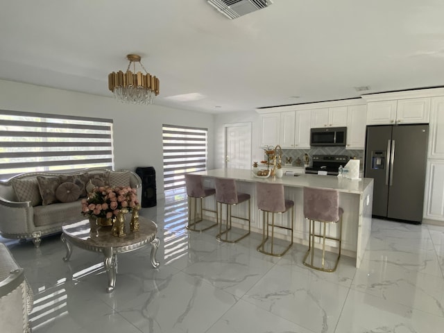 kitchen featuring tasteful backsplash, white cabinetry, a center island with sink, and appliances with stainless steel finishes