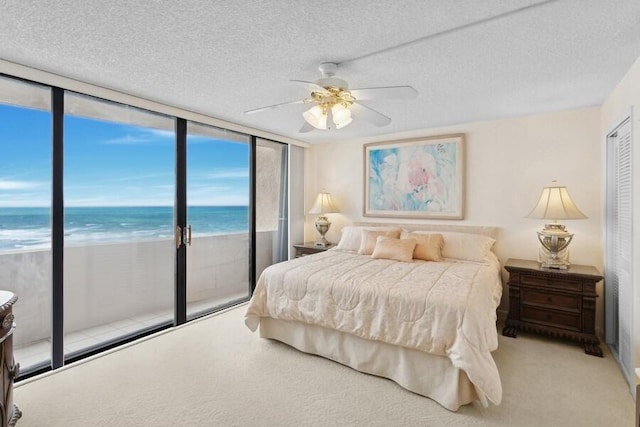 carpeted bedroom with access to exterior, ceiling fan, expansive windows, a view of the beach, and a water view