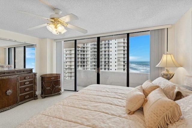 carpeted bedroom featuring ceiling fan, access to exterior, a textured ceiling, and a water view