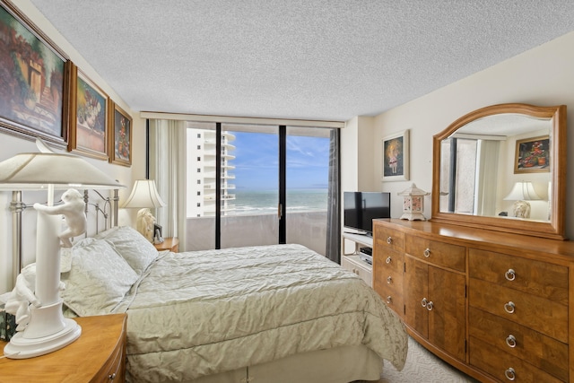 bedroom with access to outside, carpet floors, a textured ceiling, and a wall of windows