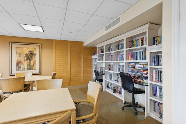 office space featuring a paneled ceiling and wood walls