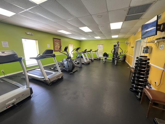 exercise room with a paneled ceiling, visible vents, and baseboards