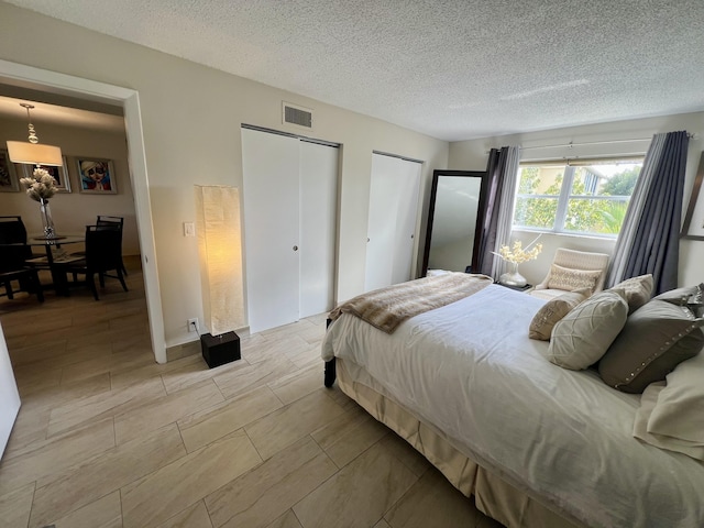 bedroom with visible vents, two closets, and a textured ceiling