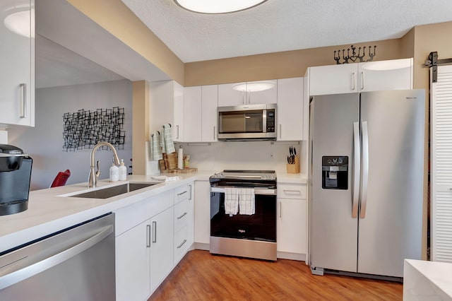 kitchen with sink, light wood-type flooring, a textured ceiling, appliances with stainless steel finishes, and white cabinetry