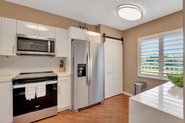 kitchen with a barn door, appliances with stainless steel finishes, a textured ceiling, white cabinets, and light wood-type flooring