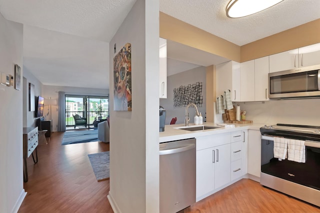 kitchen featuring appliances with stainless steel finishes, a textured ceiling, sink, light hardwood / wood-style floors, and white cabinetry