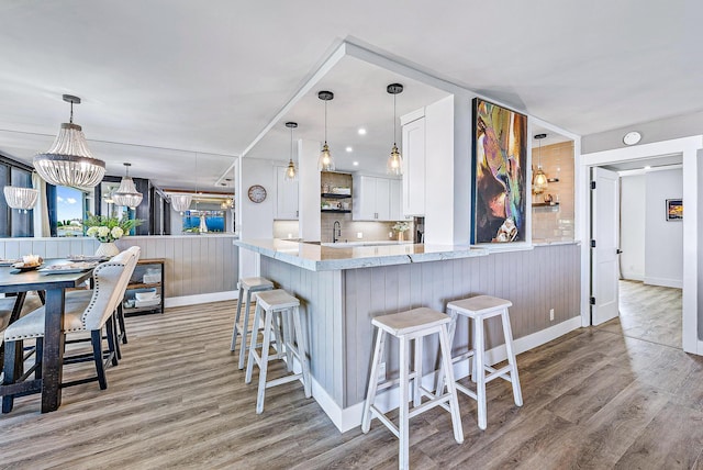 kitchen with kitchen peninsula, light wood-type flooring, decorative light fixtures, white cabinetry, and a breakfast bar area