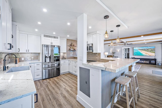 kitchen featuring white cabinets, light wood-type flooring, appliances with stainless steel finishes, decorative light fixtures, and kitchen peninsula