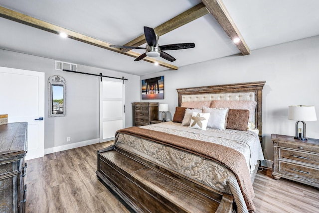 bedroom featuring ceiling fan, a barn door, beam ceiling, and light hardwood / wood-style flooring