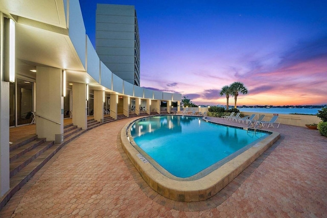 pool at dusk featuring a patio area and a water view