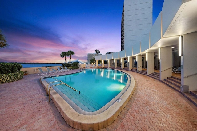 pool at dusk with a patio and a water view