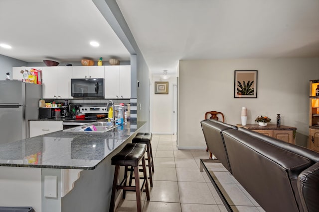 kitchen with decorative backsplash, light tile patterned floors, a kitchen bar, white cabinetry, and stainless steel appliances