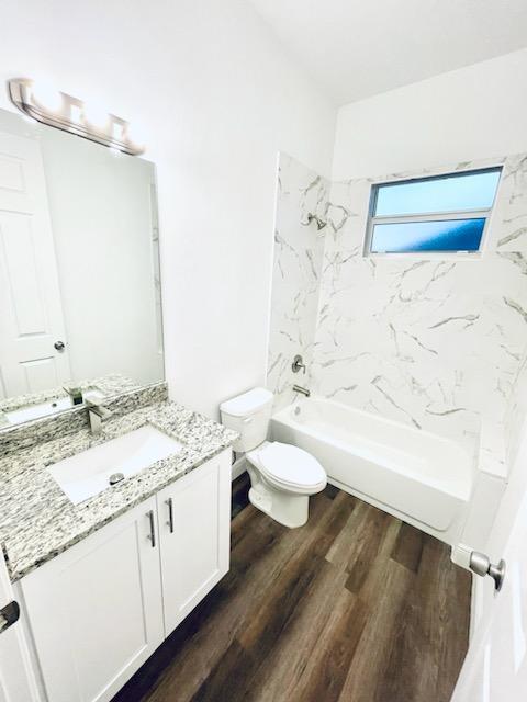 full bathroom featuring vanity, hardwood / wood-style floors, tiled shower / bath combo, and toilet