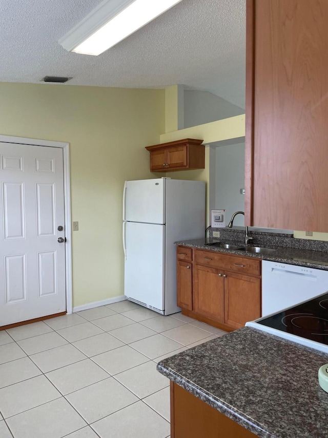 kitchen featuring sink, light tile patterned floors, white appliances, a textured ceiling, and dark stone countertops