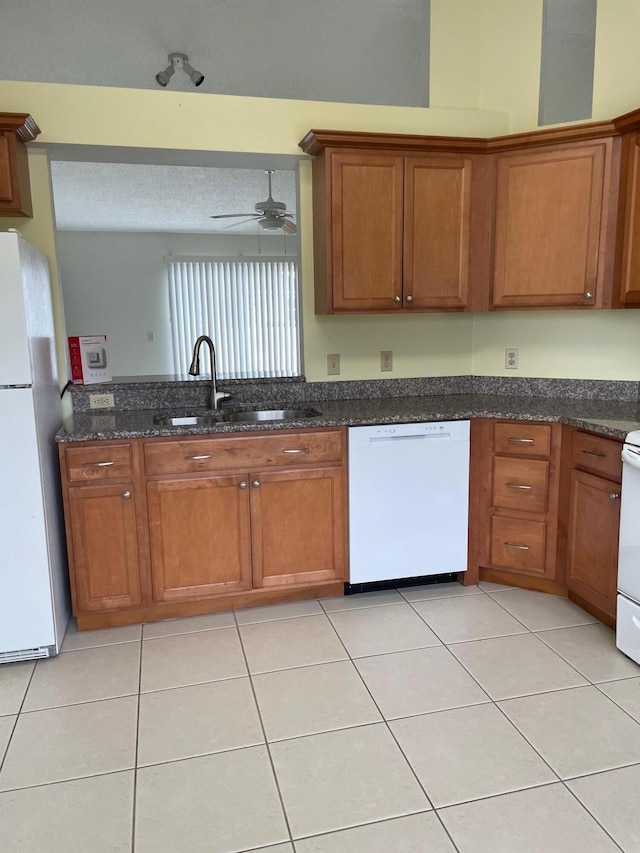 kitchen featuring sink, white appliances, light tile patterned floors, and dark stone counters