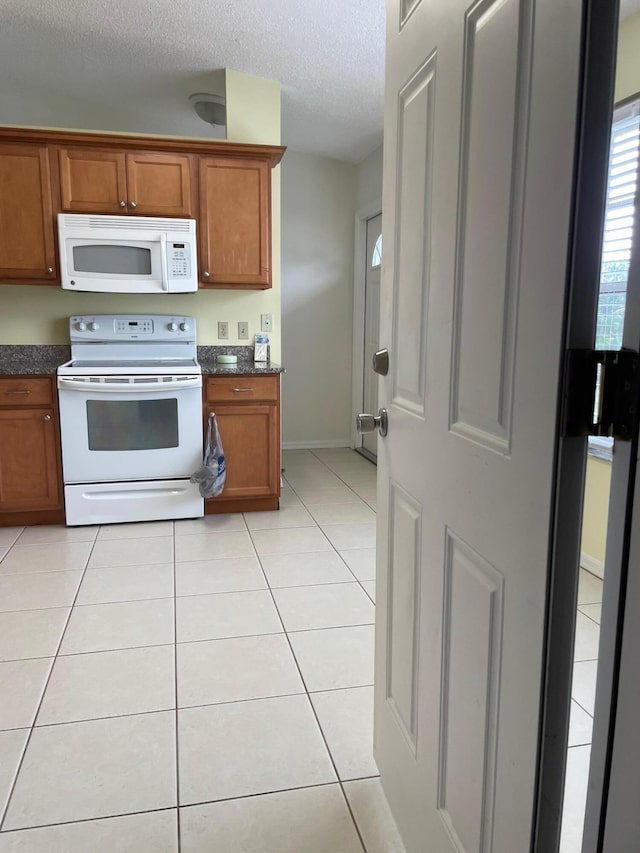 kitchen with white appliances, brown cabinetry, dark countertops, a textured ceiling, and light tile patterned flooring