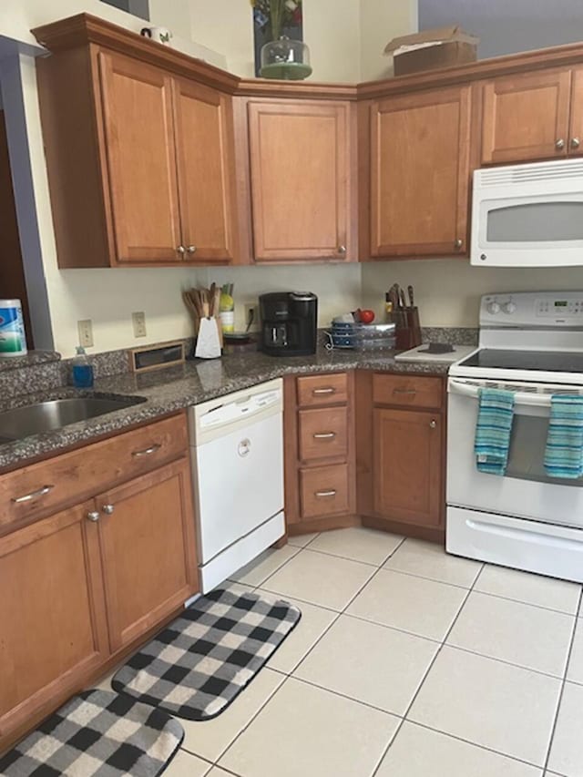 kitchen with sink, dark stone countertops, white appliances, and light tile patterned floors