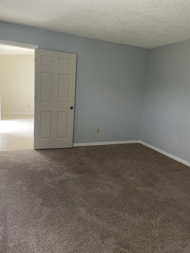 carpeted empty room with a textured ceiling, tile patterned flooring, and baseboards