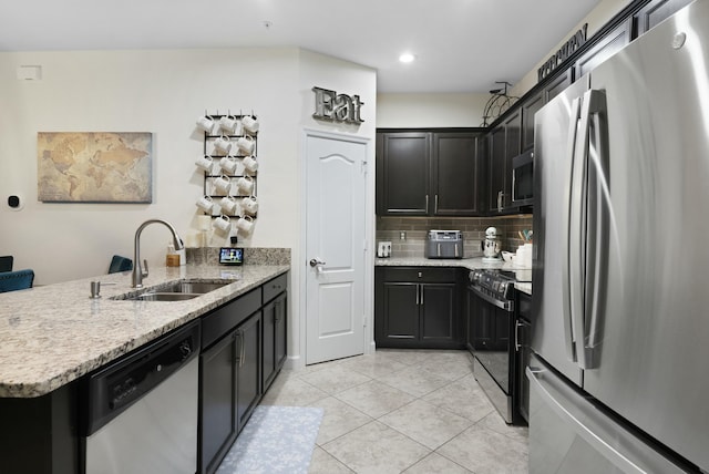 kitchen featuring sink, light stone countertops, appliances with stainless steel finishes, tasteful backsplash, and kitchen peninsula