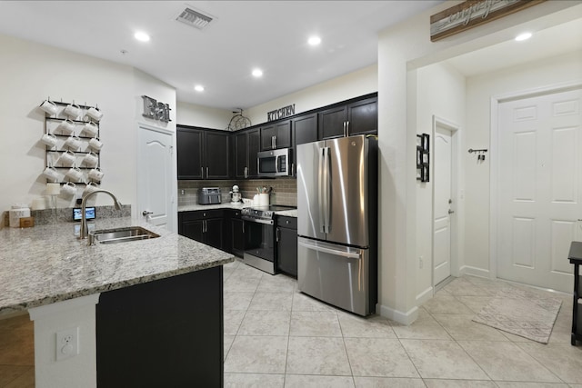 kitchen featuring light stone countertops, sink, stainless steel appliances, kitchen peninsula, and decorative backsplash